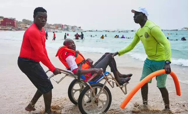 FILE - Instructors assist a participant with limited mobility out of the ocean after an aquatic therapy session in Dakar, Senegal, Saturday, Dec. 6, 2025. (AP Photo/Misper Apawu, File)
