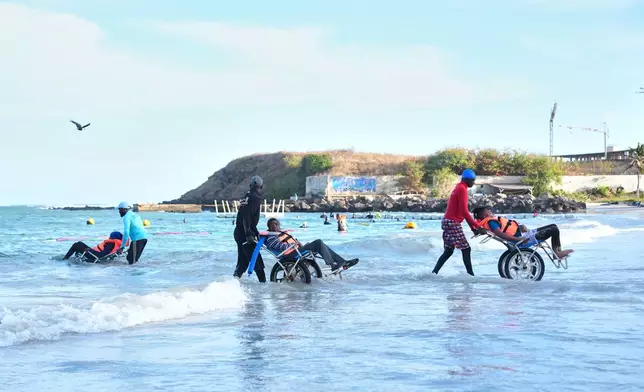FILE - Instructors assist participants with limited mobility into the ocean for an aquatic therapy session in Dakar, Senegal, Saturday, Dec. 13, 2025. (AP Photo/Misper Apawu, File)