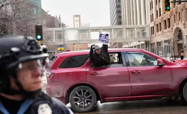 A protester holds a sign reading, "ICE Out," out of a car as she drives by Saturday, Jan. 17, 2026, in Minneapolis. (AP Photo/Yuki Iwamura)