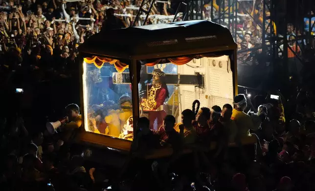 Catholic devotees walk beside a glass-covered carriage carrying the image of Jesus Nazareno during its annual procession in Manila, Philippines on its feast day on Friday Jan. 9, 2026. (AP Photo/Aaron Favila)