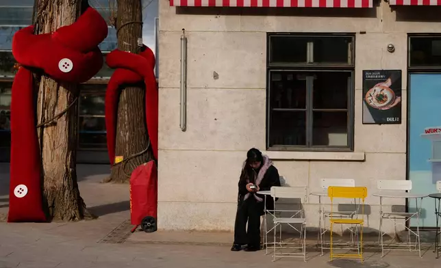 A woman looks at her smartphone outside a restaurant in Beijing, China, Thursday, Jan. 15, 2026. (AP Photo/Ng Han Guan)