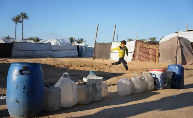A displaced Palestinian boy runs past empty water barrels as residents wait for a drinking water delivery in Deir al-Balah, Gaza Strip, Saturday, Jan. 17, 2026. (AP Photo/Abdel Kareem Hana)