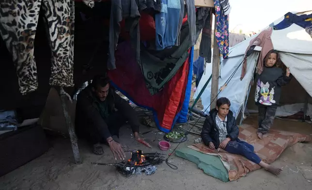 Displaced Palestinian Amr Al-Manaya, 35, sits by the fire with his children, Muhammad and Hala, next to their tent in Deir al-Balah, Gaza Strip, Saturday, Jan. 17, 2026. (AP Photo/Abdel Kareem Hana)