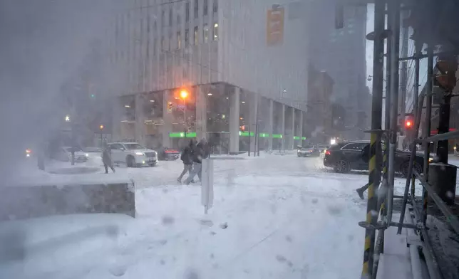 Pedestrians, obscured by snow thrown by workers cleaning a work site overhead, cross Adelaide Street along Yonge Street amid heavy snowfall and accumulation as snow and heavy winds continue to hammer the Greater Toronto Area, in Toronto, Thursday, Jan. 15, 2026. (Giordano Ciampini /The Canadian Press via AP)