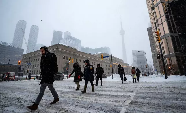 Pedestrians cross Bay Street along Front Street amid heavy snowfall and accumulation as snow and heavy winds continue to hammer the Greater Toronto Area, in Toronto, Thursday, Jan. 15, 2026. (Giordano Ciampini /The Canadian Press via AP)