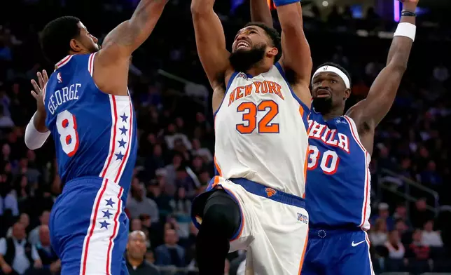 New York Knicks center Karl-Anthony Towns, middle, goes up for a shot between Philadelphia 76ers forward Paul George, left, and center Adam Bona, right, during the first half of an NBA basketball game, Saturday, Jan. 3, 2026, in New York. (AP Photo/John Munson)