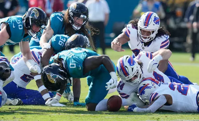 Buffalo Bills' Ray Davis, bottom right, fumbles a kickoff return from the Jacksonville Jaguars as teammate Baylon Spector (54) and Jacksonville Jaguars' Devin Lloyd (0) try to recover the ball during the first half of an NFL wild-card playoff football game Sunday, Jan. 11, 2026, in Jacksonville, Fla. (AP Photo/Chris O'Meara)