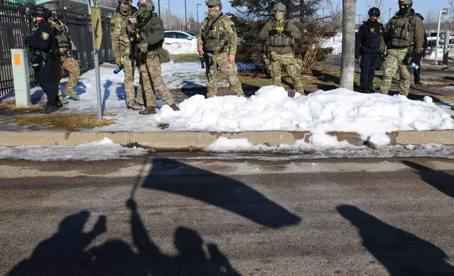 Protesters' shadows are cast on the street near law enforcement outside the Bishop Henry Whipple Federal Building in Minneapolis, Friday, Jan. 9, 2026. (AP Photo/Adam Bettcher)