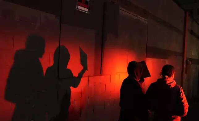 Two protesters are lit by a police light as they walk outside the U.S. Immigration and Customs Enforcement facility on Thursday, Jan. 8, 2026, in Portland, Ore. (AP Photo/Jenny Kane)