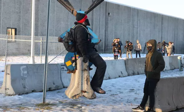 Protesters sit on a barrier that is being assembled outside the Bishop Henry Whipple Federal Building as protesters gather in Minneapolis, Friday, Jan. 9, 2026. (AP Photo/Adam Bettcher)