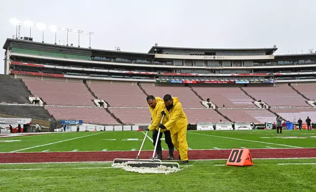 Workers clear rain water off the playing field before the Rose Bowl College Football Playoff quarterfinal game Thursday, Jan. 1, 2026, in Pasadena, Calif. (AP Photo/Kyusung Gong)