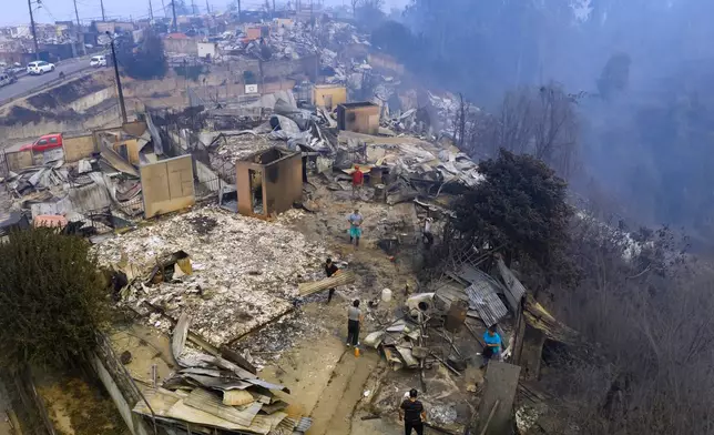 Residents stand by houses burned by wildfires in Lirquen, Chile, Sunday, Jan. 18, 2026. (AP Photo/Javier Torres)