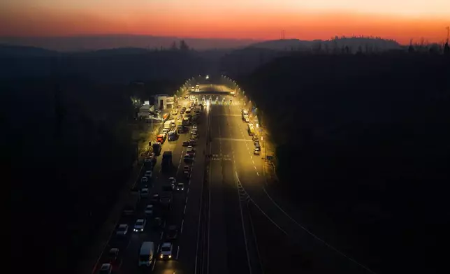 Vehicles stop at a toll plaza at sunrise as wildfires burn near Lirquen, Chile, Sunday, Jan. 18, 2026. (AP Photo/Javier Torres)