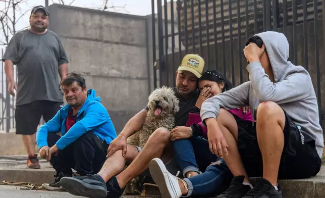 Members of the Gonzalez family sit on a sidewalk after their home caught fire during wildfires near Lirquen, Chile, Sunday, Jan. 18, 2026. (AP Photo/Javier Torres)