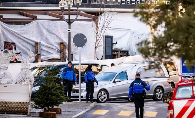A hearse drives past as police officers inspect the area where a fire broke out at the Le Constellation bar and lounge during New Year's celebration, in Crans-Montana, Switzerland, Thursday, Jan. 1, 2026. (Jean-Christophe Bott/Keystone via AP)