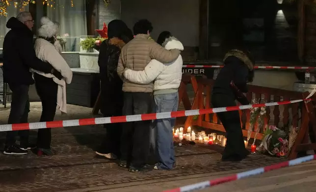 People lay candles and flowers near the Le Constellation bar, where a devastating fire left dead and injured during the New Year's celebrations in Crans-Montana, Swiss Alps, Switzerland, Thursday, Jan. 1, 2026. (AP Photo/ Antonio Calanni)