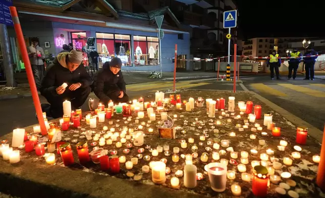 People lay candles near the Le Constellation bar, where a devastating fire left dead and injured during the New Year's celebrations in Crans-Montana, Swiss Alps, Switzerland, Thursday, Jan. 1, 2026. (AP Photo/ Antonio Calanni)