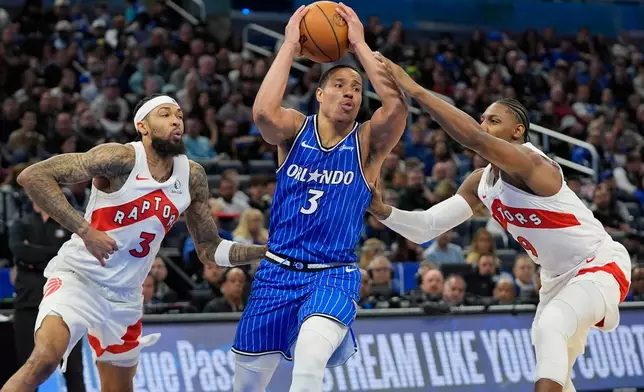 Orlando Magic guard Desmond Bane, center, drives against Toronto Raptors forward Brandon Ingram, left, and forward RJ Barrett during the first half of an NBA basketball game, Friday, Jan. 30, 2026, in Orlando, Fla. (AP Photo/John Raoux)