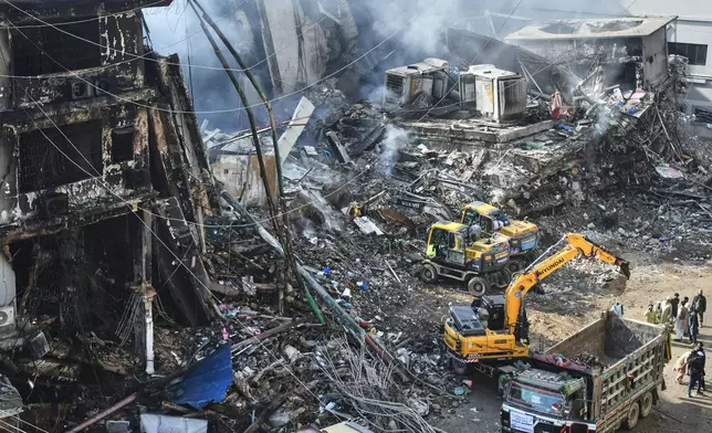 Rescue workers and firefighters use heavy machinery to clear the rubble of a burnt building of a multistory shopping plaza following a massive fire in Karachi, Pakistan, Tuesday, Jan. 20, 2026. (AP Photo/Ali Raza)