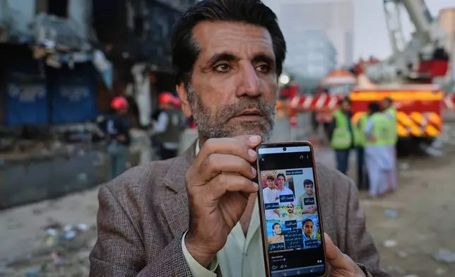 Mahmood Khan shows the press pictures of six family members who he says went missing after the fire at a multi-story shopping plaza, as he waits for information about them at the site of the fire in Karachi, Pakistan, Tuesday, Jan. 20, 2026. (AP Photo/Mohammad Farooq)