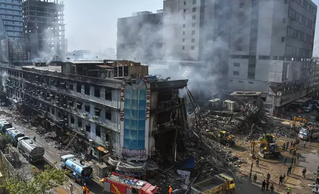 Rescue workers and firefighters work with heavy machinery to clear the rubble of a burnt building of a multi-story shopping plaza following a massive fire in Karachi, Pakistan, Tuesday, Jan. 20, 2026. (AP Photo/Ali Raza)