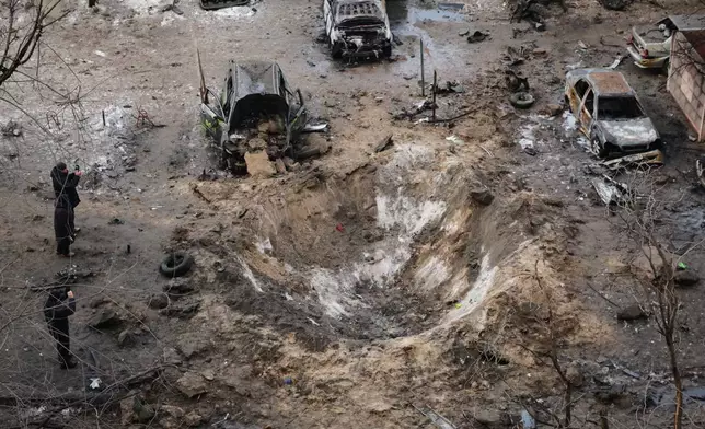 People stand near a crater and damaged cars after a Russian attack in Zaporizhzhia, Ukraine, Wednesday, Jan. 28, 2026. (AP Photo/Kateryna Klochko)