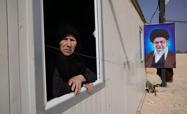 Souria al-Hassan, 75, a Syrian Shiite woman, looks out from the window of her housing unit next to a portrait of Iranian Supreme Leader Ayatollah Ali Khamenei at the Imam Ali Housing Compound, where hundreds of mostly Lebanese and Syrian Shiite Muslims displaced from Syria reside, in Hermel, northeast Lebanon, Friday, Jan. 30, 2026. (AP Photo/Hussein Malla)
