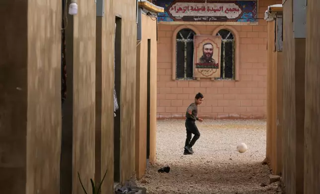 A Syrian Shiite boy, plays with a ball in front of a portrait of the late top Hezbollah military commander Imad Mughniyeh at the Imam Ali Housing Compound, where hundreds of mostly Lebanese and Syrian Shiite Muslims displaced from Syria reside, in Hermel, northeast Lebanon, Friday, Jan. 30, 2026. (AP Photo/Hussein Malla)