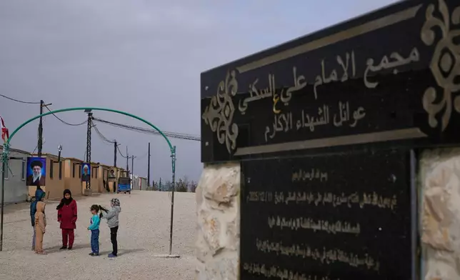 Syrian Shiite girls gather at the Imam Ali Housing Compound, where hundreds of mostly Lebanese and Syrian Shiite Muslims displaced from Syria reside, in Hermel, northeast Lebanon, Friday, Jan. 30, 2026. The Arabic words right, read:"The Imam Ali Housing Compound, families of the honorable martyrs." (AP Photo/Hussein Malla)