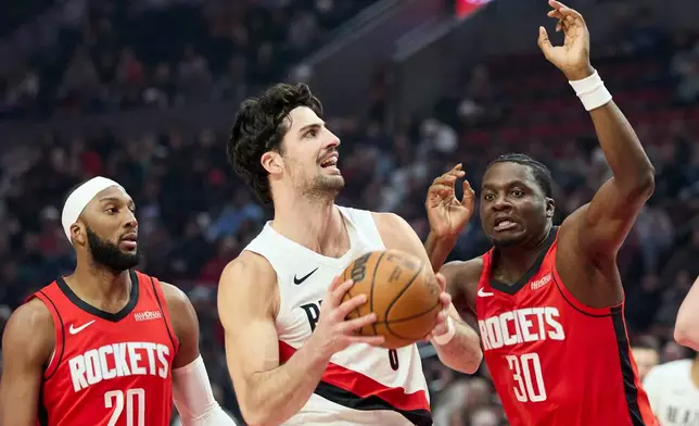 Portland Trail Blazers forward Deni Avdija, center, drives to the basket between Houston Rockets center Clint Capela, right, and guard Josh Okogie during the first half of an NBA basketball game in Portland, Ore., Wednesday, Jan. 7, 2026. (AP Photo/Craig Mitchelldyer)