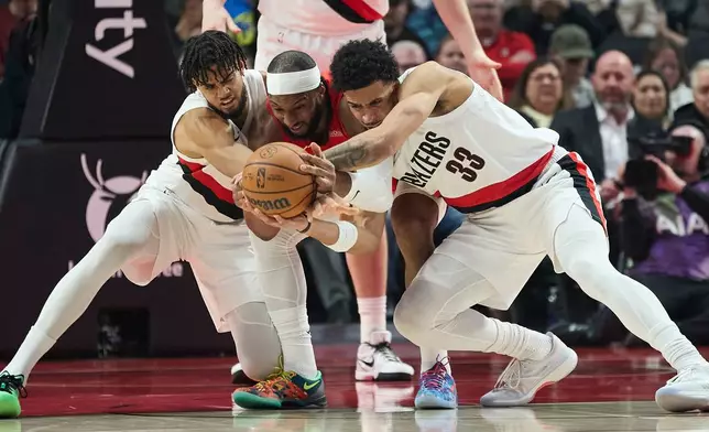 Houston Rockets guard Josh Okogie, center, fights for the ball with Portland Trail Blazers forward Rayan Rupert, left, and forward Toumani Camara during the first half of an NBA basketball game in Portland, Ore., Wednesday, Jan. 7, 2026. (AP Photo/Craig Mitchelldyer)