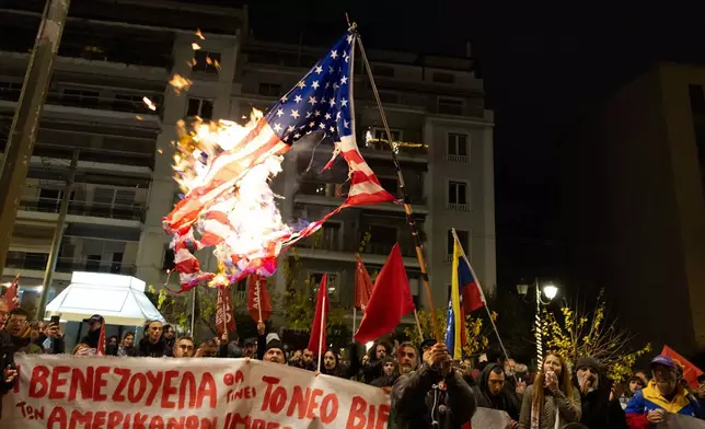 A protester raises a US flag which has been set ablaze during a rally opposing the United States strikes on Venezuela and the capturing of its President Nicolas Maduro, outside the U.S embassy in Athens, Greece, Saturday, Jan. 3, 2026. (AP Photo/Yorgos Karahalis)