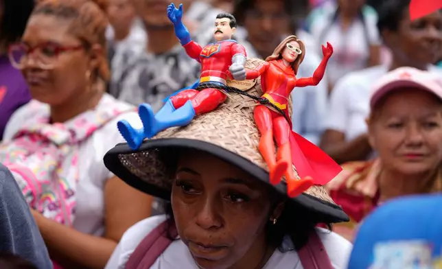 A government supporter wears a hat with dolls from the TV program, Super Bigote, based on President Nicolas Maduro and first lady Cilia Flores, during a protest demanding their release from U.S. custody, in Caracas, Venezuela, Sunday, Jan. 4, 2026. (AP Photo/Ariana Cubillos)