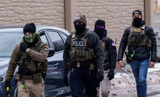 Immigration and Customs Enforcement (ICE) agents, including one wearing a 'NOT ICE' face covering, walk near their vehicles, Thursday, Jan. 15, 2026, in Richfield, Minn. (AP Photo/Adam Gray)