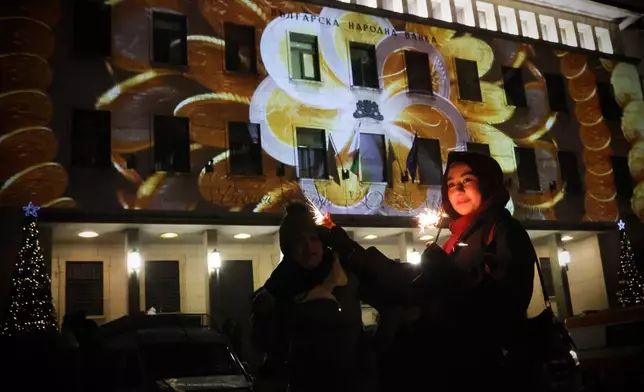 A woman holds sparklers during the celebration of the New Year and Bulgaria's adoption of euro in front of Bulgarian National Bank in Sofia, enlighten by Euro coins projection, Thursday Jan. 1, 2026. (AP Photo/Valentina Petrova)