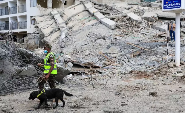 A police officer with a sniffer dog searches for survivors following the collapse of a building in Nairobi, Kenya, Friday, Jan. 2, 2026. (AP Photo/Andrew Kasuku)