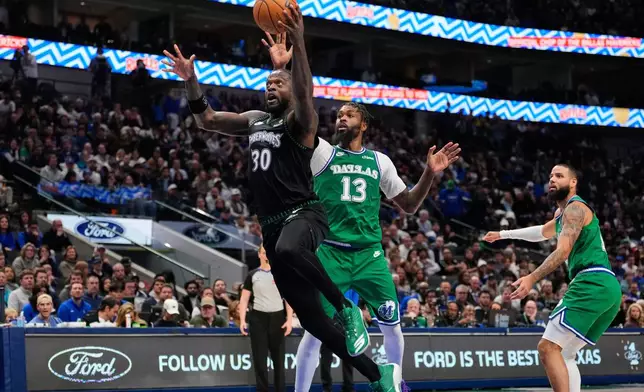 Minnesota Timberwolves forward Julius Randle (30) leaps to the basket for a shot after getting past Dallas Mavericks' Naji Marshall (13) and Caleb Martin, right, in the first half of an NBA basketball game Wednesday, Jan. 28, 2026, in Dallas. (AP Photo/Tony Gutierrez)