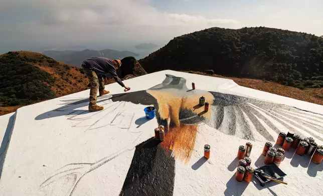 Rob Aspire paints a Long-tailed Shrike on the rooftop of a stone house on Sunset Peak, Lantau, Hong Kong on Jan. 25, 2025. (AP Photo/May James)