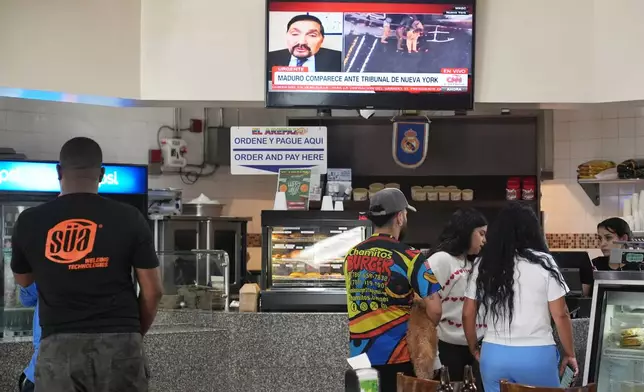 People order food at El Arepazo, a popular restaurant in the local Venezuelan community, as a television broadcast shows Venezuelan President Nicolas Maduro being led from a helicopter to a court appearance in New York, Monday, Jan. 5, 2026, in Doral, Fla. (AP Photo/Lynne Sladky)