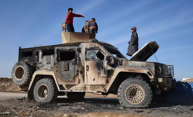 Local youth play atop of a damaged armored vehicle belonging to the Syrian Democratic Forces (SDF) at the site of clashes with Syrian government forces in the village of al-Hol in northeastern Syria's Hasakeh province, Syria, Wednesday, Jan. 21, 2026. (AP Photo/Ghaith Alsayed)