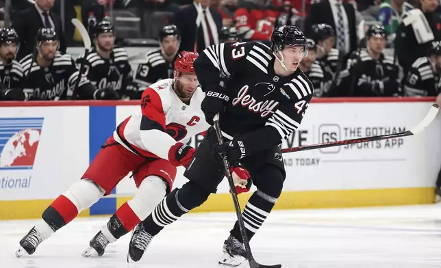 New Jersey Devils defenseman Luke Hughes (43) skates with the puck past Carolina Hurricanes center Jordan Staal (11) during the first period of an NHL hockey game Saturday, Jan. 17, 2026, in Newark, N.J. (AP Photo/Adam Hunger)