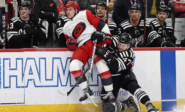 New Jersey Devils left wing Paul Cotter (47) checks Carolina Hurricanes center Sebastian Aho (20) in front of the Devils bench during the first period of an NHL hockey game Saturday, Jan. 17, 2026, in Newark, N.J. (AP Photo/Adam Hunger)