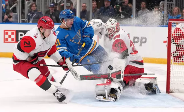 Carolina Hurricanes goaltender Brandon Bussi (32) deflects a puck as teammate Carolina Hurricanes' Alexander Nikishin, left, and St. Louis Blues' Jimmy Snuggerud, center, watch during the second period of an NHL hockey game Tuesday, Jan. 13, 2026, in St. Louis. (AP Photo/Jeff Roberson)