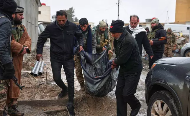 Syrian government soldiers and locals carry the body of a dead civilian found by relatives in the street after government forces seized the strategic town of Taqba in eastern Syria, as part of an ongoing push against Kurdish-led forces, Sunday, Jan. 18, 2026. (AP Photo/Ghaith Alsayed)