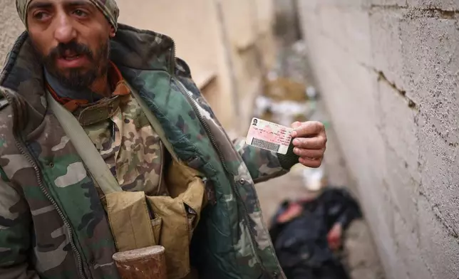 A Syrian government soldier displays the ID of a dead civilian found in the street after government forces seized the strategic town of Taqba in eastern Syria, as part of an ongoing push against Kurdish-led forces, Sunday, Jan. 18, 2026. (AP Photo/Ghaith Alsayed)