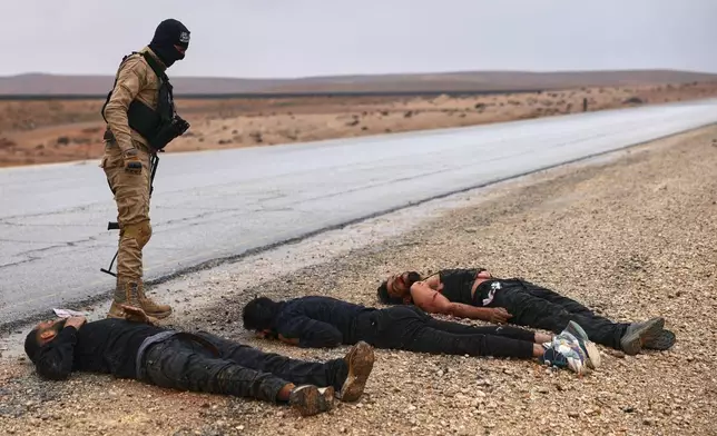 A Syrian government soldier stands next to the bodies of U.S.-backed Syrian Democratic Forces (SDF) fighters on a road leading to the strategic town of Taqba in eastern Syria, during an ongoing push against Kurdish-led forces, Sunday, Jan. 18, 2026. (AP Photo/Ghaith Alsayed)