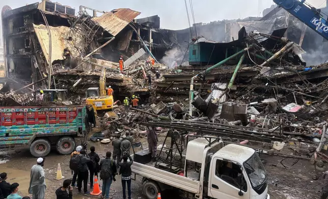 Rescue workers and firefighters work with heavy machinery to search through the rubble of a burnt building of a multistory shopping plaza following a massive fire in Karachi, Pakistan, Monday, Jan. 19, 2026. (AP Photo/Mohammad Farooq)
