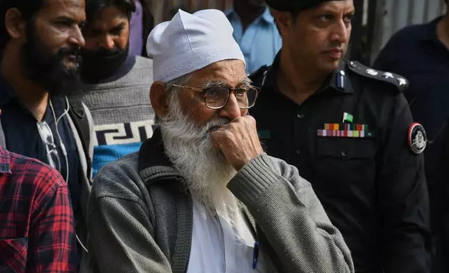 Family members of missing persons wait near the site of a burnt building of a multistory shopping plaza following a massive fire in Karachi, Pakistan, Monday, Jan. 19, 2026. (AP Photo/Ali Raza)