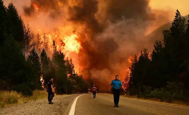 People walk on a road as a wildfire blazes in El Hoyo, Patagonia, Argentina, Thursday, Jan. 8, 2026. (AP Photo/Maxi Jonas)