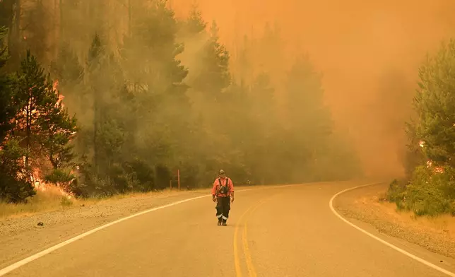 A firefighter walks on a road as wildfires blaze in El Hoyo, Patagonia, Argentina, Thursday, Jan. 8, 2026. (AP Photo/Maxi Jonas)